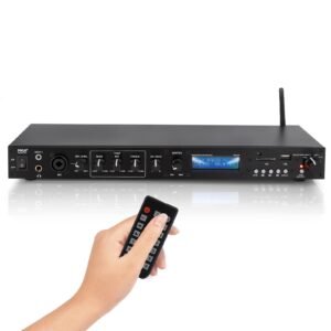Black audio receiver with remote control in hand, radio display visible